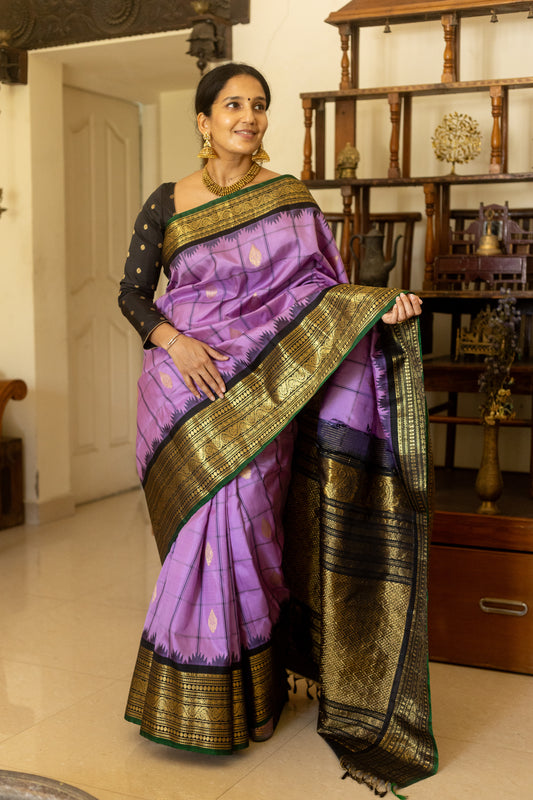 Woman in a purple saree with gold border indoors