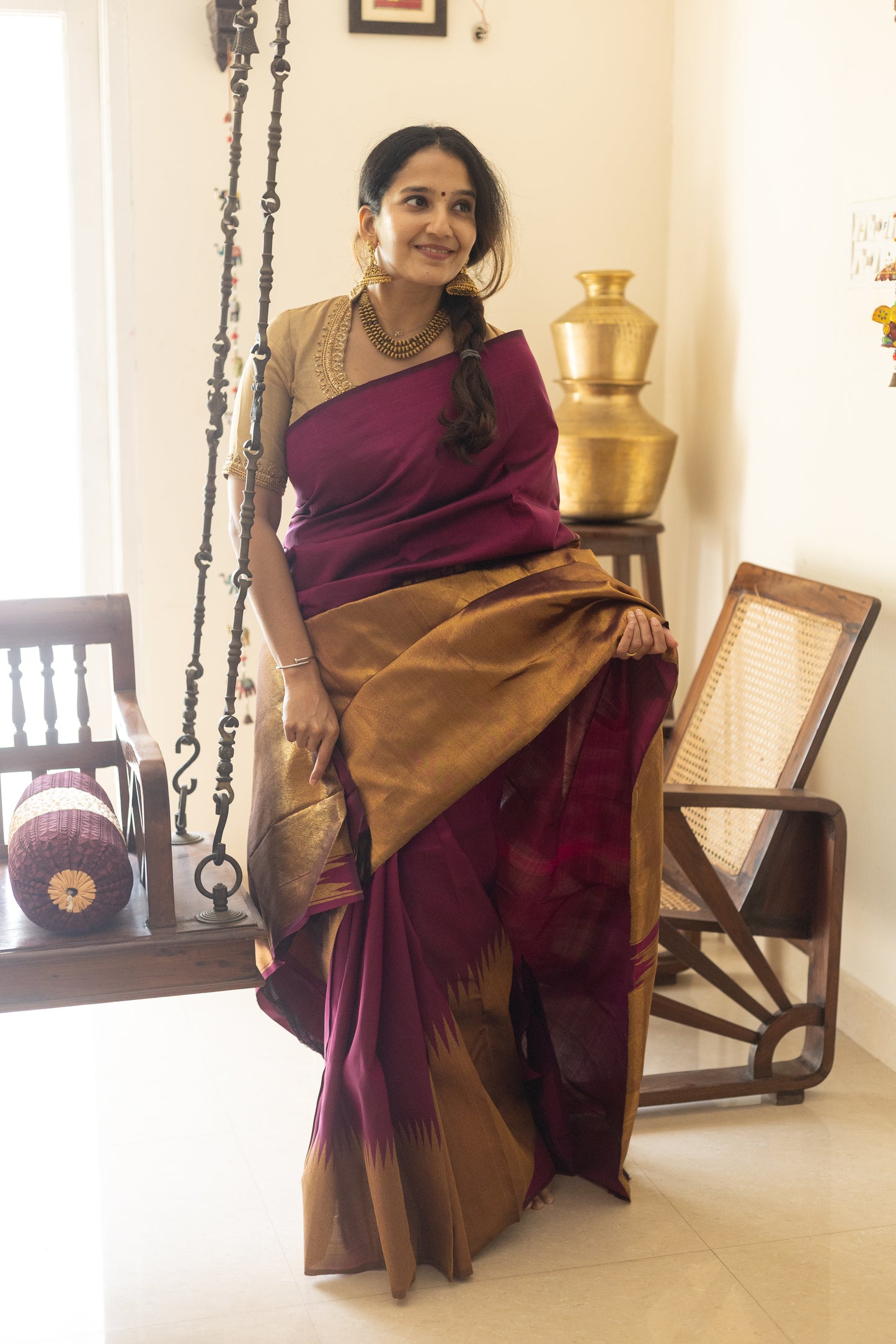 Woman in a traditional maroon and gold saree sitting indoors.