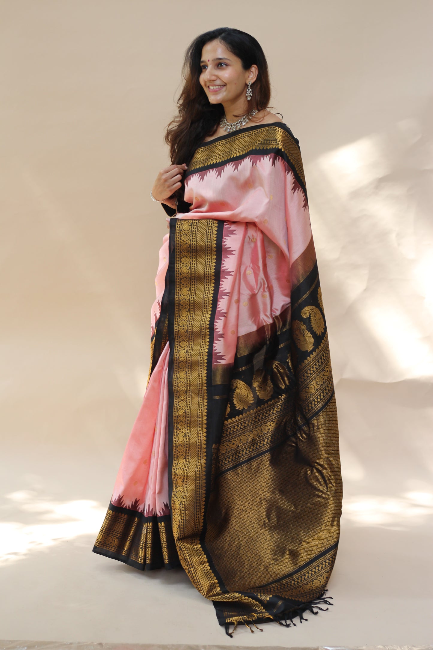 Woman holding a traditional saree with a gold and pink design against a plain background